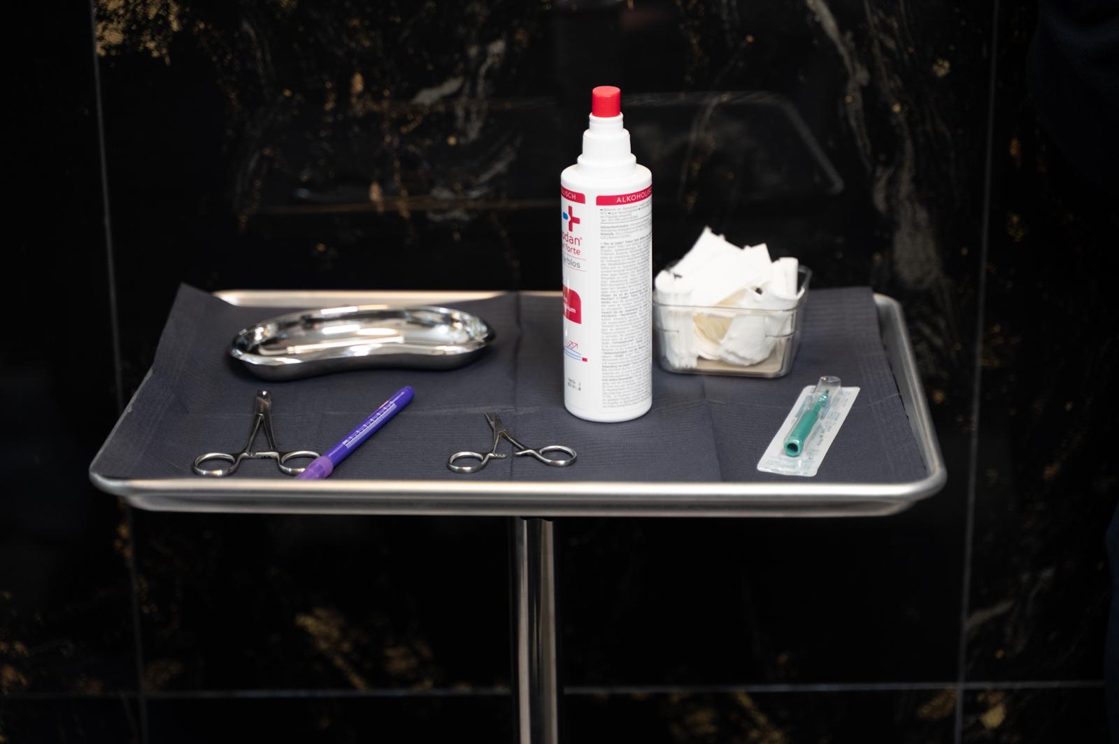 Steril vorbereitetes Piercing-Setup: Instrumente, Desinfektion, sterile Tupfer und verpackte Einwegnadel auf dem Tray